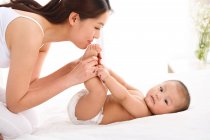 Vista lateral de feliz joven madre jugando con adorable pequeño bebé en casa - foto de stock