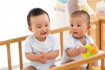 Zwei entzückende glückliche chinesische Babys sitzen zusammen in der Krippe — Stockfoto