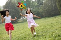 Dos chicas jugando con molino de viento de papel - foto de stock