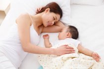 Blick von oben auf eine glückliche junge Mutter, die ihr entzückendes Baby ansieht, das auf dem Bett schläft — Stockfoto