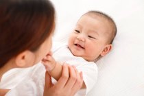 Cropped shot of happy young mother playing with adorable little baby lying on bed — Stock Photo