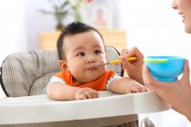 Cropped shot of mother holding spoon and feeding adorable little baby — Stock Photo