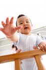 Low angle view of adorable asian baby standing in crib and looking at camera — Stock Photo
