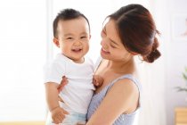 Feliz joven madre sosteniendo adorable alegre bebé en casa - foto de stock