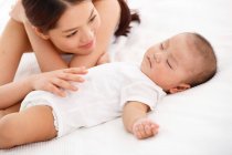 Junge Mutter schaut entzückendes Baby an, das im Bett schläft — Stockfoto