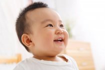 Primer plano vista de adorable feliz asiático bebé niño riendo y mirando hacia otro lado - foto de stock