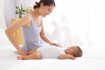 Heureuse jeune mère regardant adorable bébé dormir sur le lit — Photo de stock