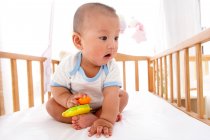 Close-up view of adorable asian baby boy sitting in crib and looking away — Stock Photo