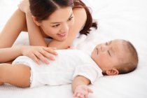 Junge Mutter schaut entzückendes Baby an, das im Bett schläft — Stockfoto