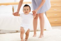 Cropped shot of young mother learning adorable little baby to walk at home — Stock Photo