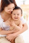 Glückliche junge Mutter umarmt entzückendes kleines Baby zu Hause — Stockfoto