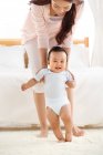 Счастливая молодая мама учит очаровательного малыша гулять дома — стоковое фото