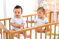 Два милых счастливых азиатских ребенка сидят вместе в кроватке — стоковое фото