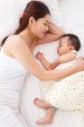 Vue grand angle de la jeune mère regardant bébé adorable dormir sur le lit — Photo de stock