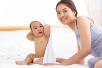 Glückliche junge Mutter und süßes Baby mit Handtuch auf dem Kopf zu Hause — Stockfoto