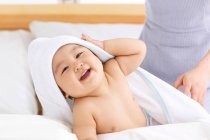 Cropped shot of mother standing near adorable happy baby lying on bed — Stock Photo