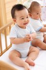 Two adorable happy asian babies sitting together in crib — Stock Photo