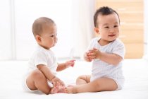Two adorable happy chinese babies sitting together on bed — Stock Photo