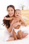 Heureuse jeune mère étreignant bébé mignon et souriant à la caméra — Photo de stock