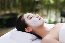 Jeune femme asiatique avec les yeux fermés couché avec masque facial au spa extérieur — Photo de stock