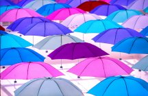 Bright colorful umbrellas hanging on light background, full frame view — Stock Photo