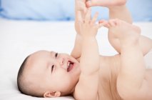 Cute baby lying in bed holding his toes — Stock Photo