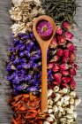 Вид зверху на сушені квіти, чайне листя і дерев'яна ложка на столі — стокове фото