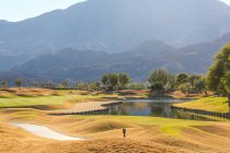 Удивительный зеленый газон на поле для гольфа, озеро и красивые горы в солнечный день — стоковое фото