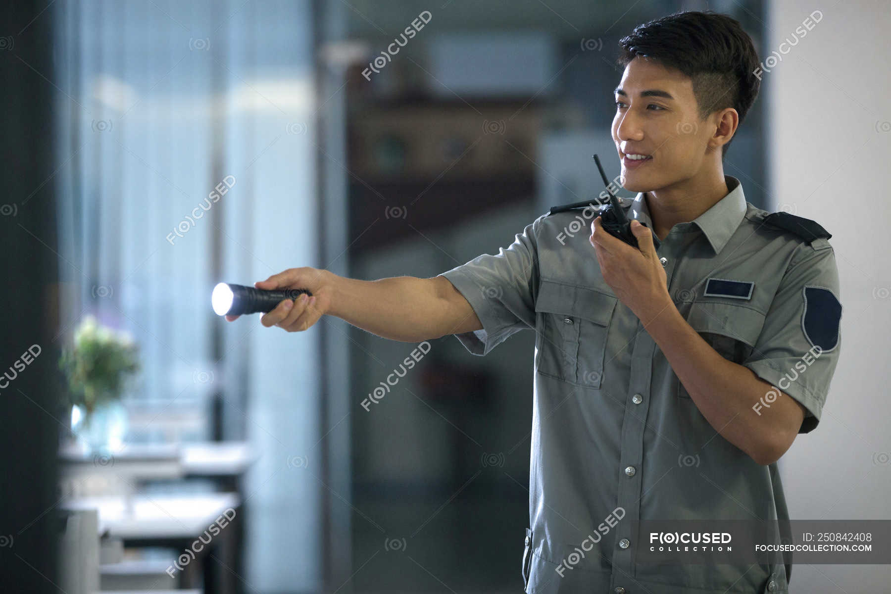 Smiling Young Security Guard Holding Flashlight And Using Walkie Talkie