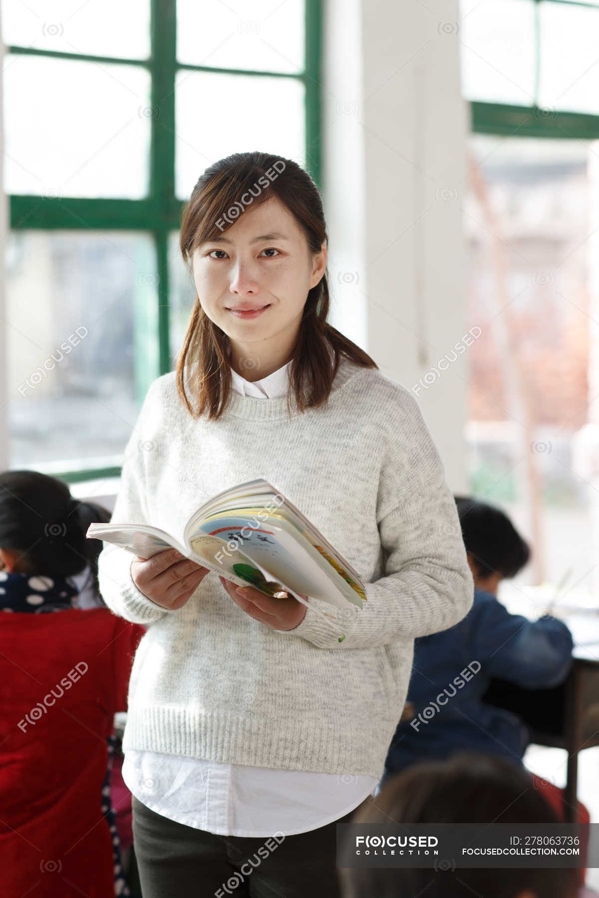 Rural female teacher smiling at camera while pupils studying in ...