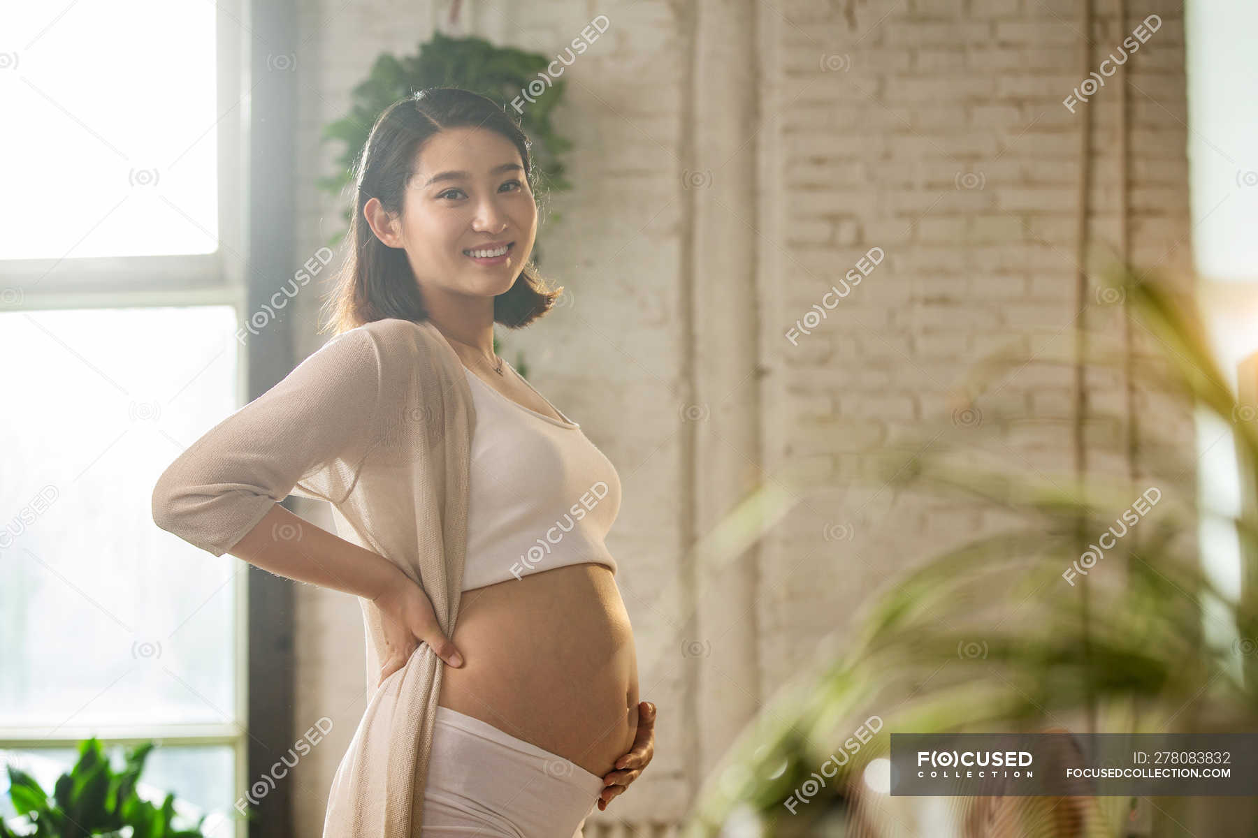 side-view-of-young-pregnant-asian-woman-smiling-at-camera-while