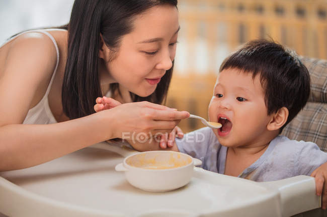 Happy young asian mommy feeding adorable toddler at home — Stock Photo