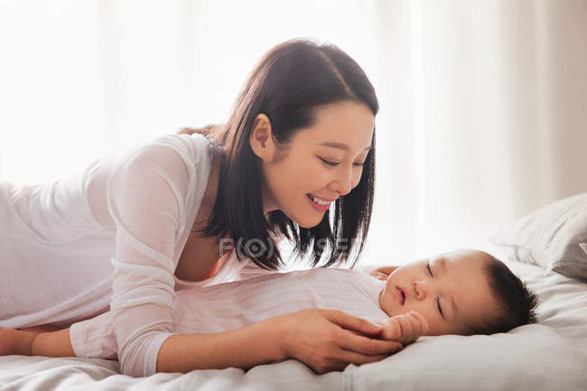 Щаслива молода мати дивиться на чарівну дитину, що спить на ліжку — стокове фото