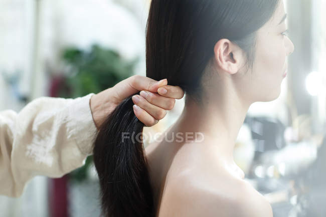 Plan recadré de femme faisant coiffure à belle jeune fille asiatique dans le salon de beauté — Photo de stock