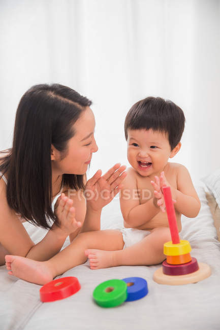 Happy young mother looking at adorable toddler playing with colorful toy at home — Stock Photo