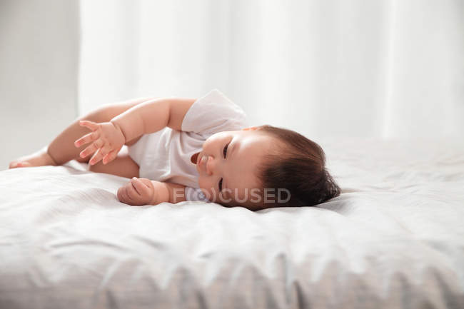 Чарівна азіатська дитина лежить на ліжку з білими постільними речами вдома — стокове фото
