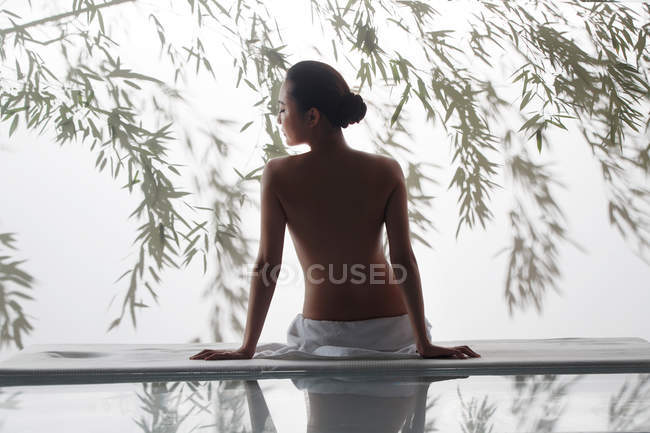 Back view of beautiful naked woman sitting on massage table in spa — Stock Photo