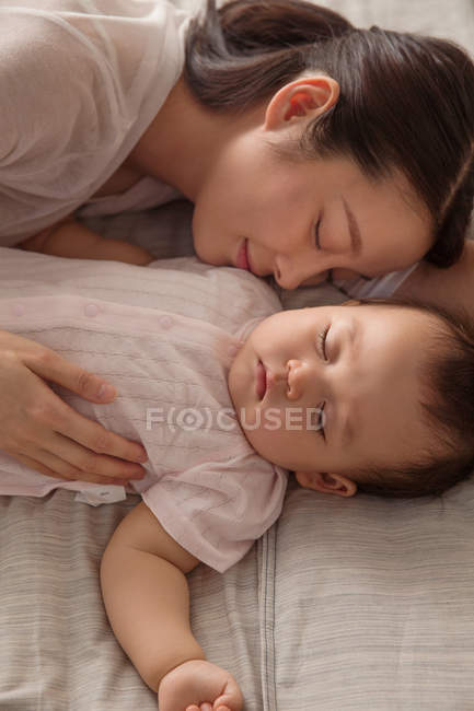 Vista dall'alto di sorridere giovane madre dormire con adorabile bambino sul letto — Foto stock