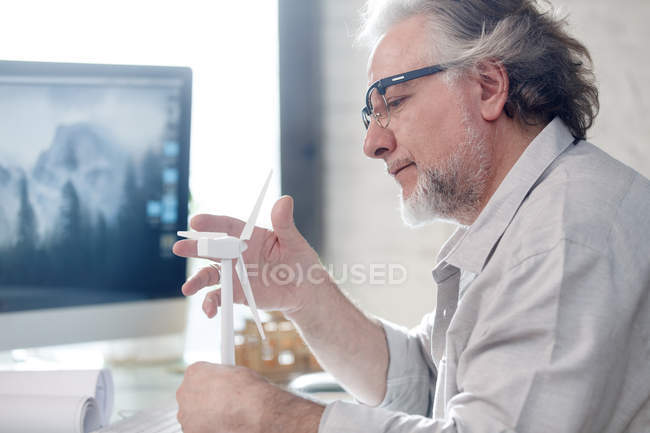 Side view of serious professional mature architect in eyeglasses holding windmill model at workplace — Stock Photo