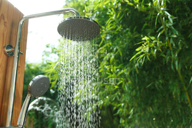 Vista de cerca de la ducha con agua que cae y fondo natural verde - foto de stock