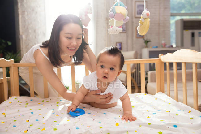 Happy young mother carrying beautiful infant crawling in crib — Stock Photo