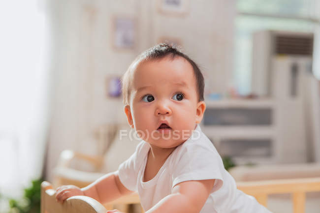 Здивована маленька азіатська дитина спирається на дитяче ліжечко і дивиться вдома — стокове фото