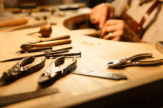 Зменшеному вигляді інструменти на дерев'яний стіл і дизайнер ювелірних виробів, що працюють позаду, кадроване постріл — стокове фото