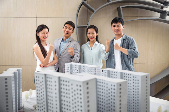 Professional happy young team of architects standing together near project and smiling at camera in office — Stock Photo