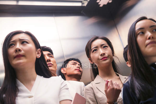 Vista basso angolo di gravi giovani uomini d'affari asiatici e donne d'affari in piedi insieme in ascensore — Foto stock