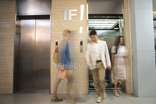 Borrosa asiático negocios personas caminando cerca ascensor en moderno oficina - foto de stock