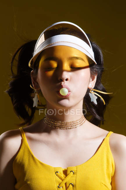Bela asiática menina no cap e estrela em forma de brincos soprando chiclete no estúdio — Fotografia de Stock
