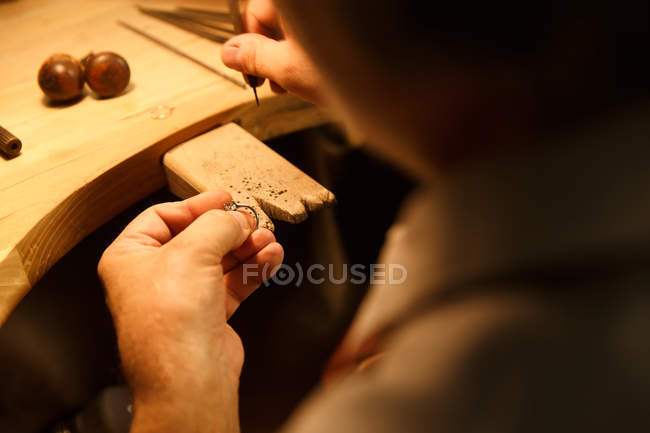 Обрезанный снимок мужчины ювелира, работающего с кольцом в мастерской, вид через плечо, избирательный фокус — стоковое фото