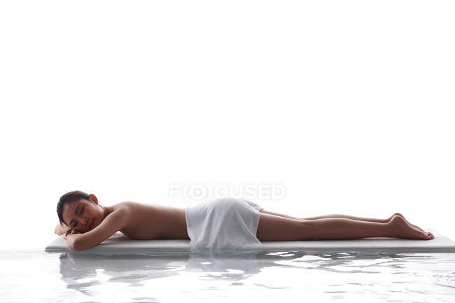 Side view of beautiful asian woman with closed eyes lying with towel on body in spa — Stock Photo