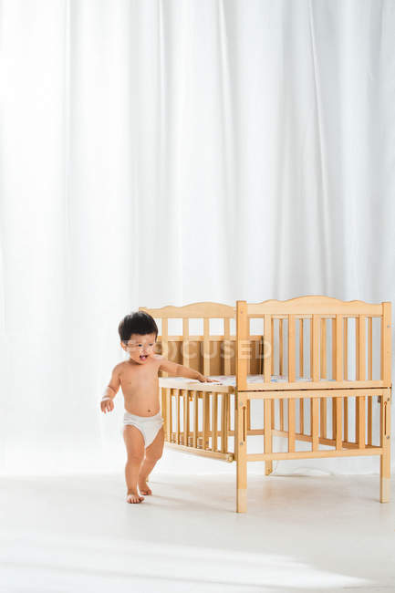 Adorable bébé heureux en couches marchant près de la crèche dans la chambre — Photo de stock